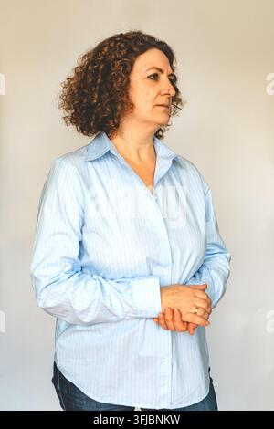 Ritratto di una donna matura con capelli ricci in una camicia blu dall'aria pensierosa Foto Stock