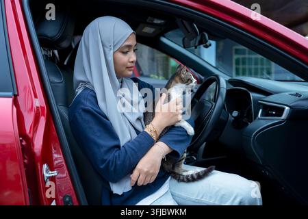 Giovane donna seduta su un'auto con gatto Foto Stock