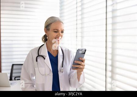 Medica sorridente che utilizza uno smartphone nell'ufficio della clinica Foto Stock