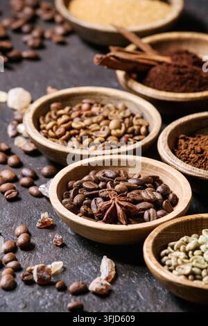 Varietà di messa a terra, il caffè istantaneo, diversi i chicchi di caffè e lo zucchero di canna, spezie in ciotole di legno scuro su sfondo di texture. Close up Foto Stock