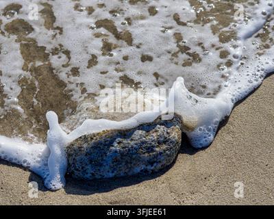 Onda schiumosa dell'oceano che si riversa su un piccolo scoglio sulla spiaggia di Ardore in Italia Foto Stock