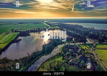 Dron che cattura un'estesa paesaggio di polder con terreni agricoli verdi, corpi d'acqua e edifici residenziali sotto un cielo dell'ora dorata a Zoeterwoude Dorp Foto Stock