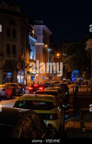 Molte auto che circolano e parcheggiano nel traffico urbano su una strada storica di Bucarest per raggiungere l'area centrale di notte Foto Stock