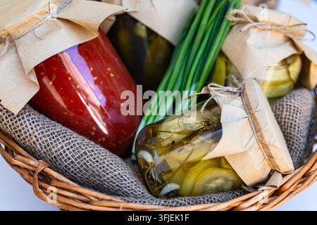 Conserve di verdure fatte in casa assortite in barattoli di vetro rustici e un cesto di vimini Foto Stock