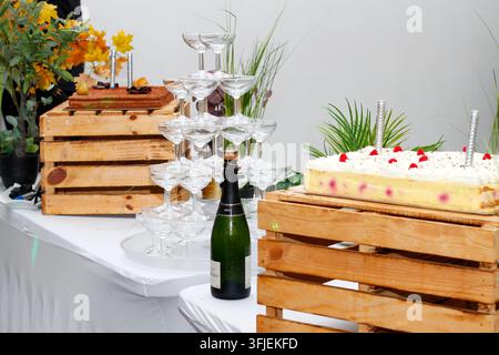 Bicchieri impilati con bottiglia e torte decorate su casse di legno a un buffet di festa Foto Stock