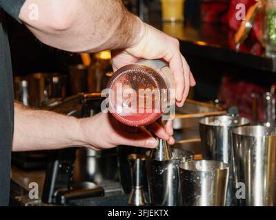 Barista che versa un liquido da una bottiglia in un misurino sopra dei shakers per cocktail in metallo in un bar. Foto Stock