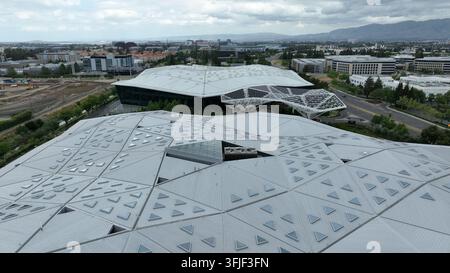 Sede centrale di Nvidia con tetto iconico a facce diamantate sopra la facciata in vetro, viale con traffico in primo piano e l’espansione della Silicon Valley con montagne Foto Stock