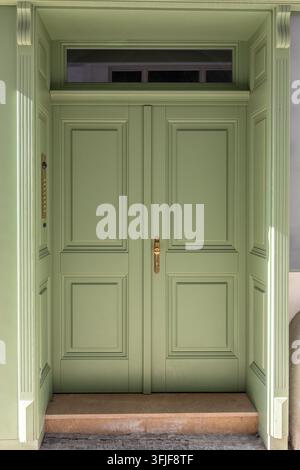 Porte doppie verde pallido con pannelli decorativi, maniglia in ottone e finestra a transetto. Foto Stock