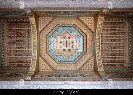 Soffitto in legno dipinto al Palazzo Bahia di Marrakesh, Marocco, con intricati lavori di piastrelle geometriche, dettagli in gesso intagliato e ornamenti riccamente decorati Foto Stock