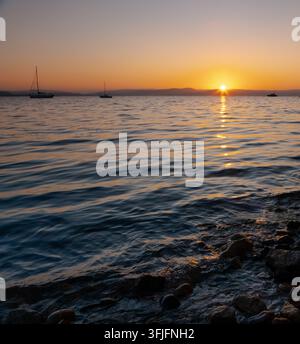 Veduta tranquilla del mare con yacht e barche a vela ancorati in mare durante un'alba dorata con riflessi del sole sull'acqua increspata a Mumbles, Swansea Foto Stock