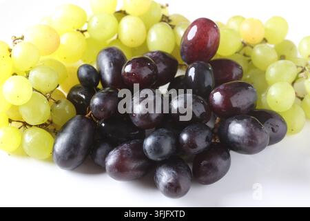 Grappoli di uva fresca verde e viola scuro appoggiati su una superficie di piatto bianco Foto Stock