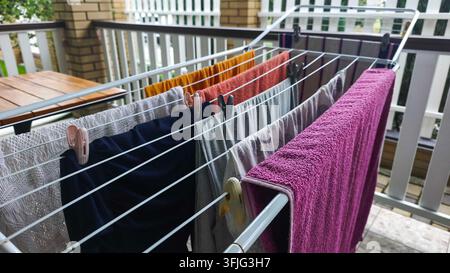 Stendipanni tiene vestiti scuri e colorati con mollette di legno sulla terrazza. Il bucato asciuga all'aria fresca, mentre lo stendipanni evidenzia la cura domestica, fabr Foto Stock