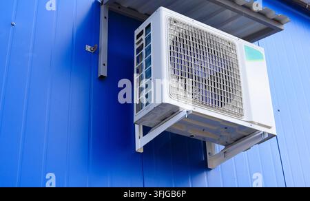 Unità di condizionatore su un muro di edificio. L'unità esterna del condizionatore è montata su un muro blu. Unità esterna di un condizionatore e ventilazione Foto Stock