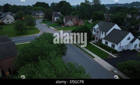 Scena del crepuscolo in una zona residenziale nobile con grandi case unifamiliari. Quartiere periferico di una città americana in estate. Incrocio con cartello di stop sulla strada. Vista aerea Foto Stock