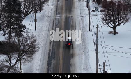 Vista aerea invernale di una carrozza trainata da cavalli che percorre una strada rurale innevata e ghiacciata in Pennsylvania. I mezzi di trasporto tradizionali degli Amish si muovono attraverso la quiete Foto Stock