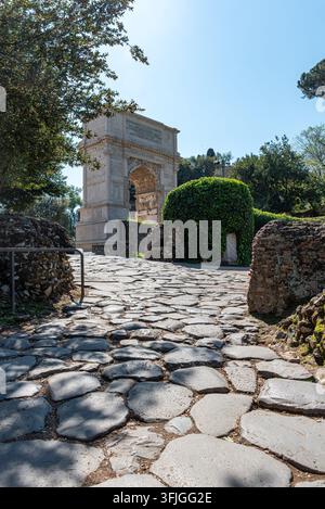 Una fotografia atmosferica che mostra l'arco storico di Tito accompagnato da una tipica strada romana lastricata di ciottoli che conduce direttamente verso Foto Stock