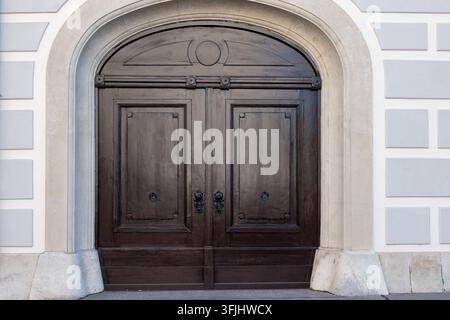 Una doppia porta in legno scuro si trova all'interno di un ingresso in pietra ad arco su una facciata chiara. Foto Stock