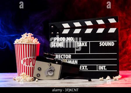 Concetto di cinema e produzione cinematografica, ciak con macchina fotografica vintage e secchio di popcorn su tavolo di legno con sfondo di fumo blu e rosso Foto Stock
