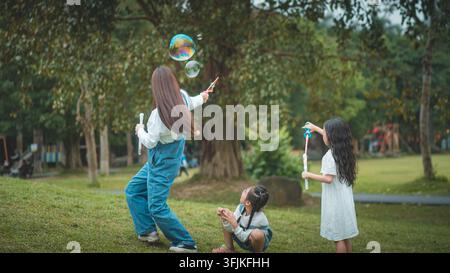 Donna che soffia bolle di sapone con due ragazze sul prato di un parco, Ecopark, Hanoi, Vietnam Foto Stock