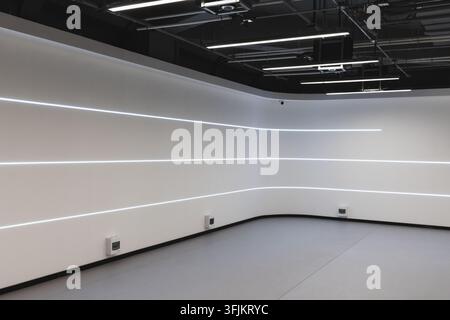 Studio interno minimalista futuristico con pareti bianche curve e strisce luminose LED orizzontali, soffitto industriale esposto e pavimento aperto. Pulito, moderno g Foto Stock