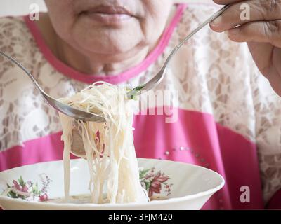 Primo piano, donna anziana asiatica mangia noodles istantanei, junk food, persona anziana che mangia noodles istantanei, pericoli delle diete ad alto contenuto di sodio, rischio di malattie cardiache. Foto Stock