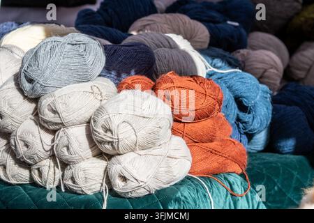 Un mucchio di gomitoli di lana disposti su una superficie coperta da un tessuto verde, con piccoli gomitoli nelle tonalità di beige-avorio, arancione e grigio chiaro Foto Stock