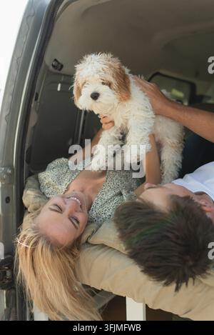 Giovane coppia felice che gioca con un cucciolo in un camper durante un viaggio Foto Stock