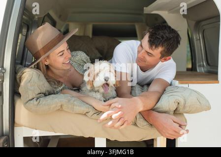 Coppia felice con il cane domestico sdraiata nel camper durante un viaggio su strada Foto Stock