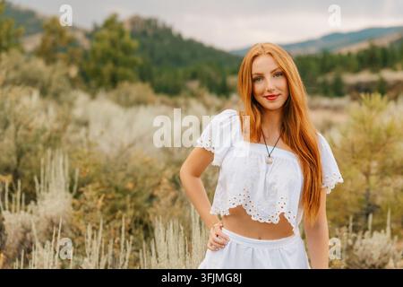 Giovane donna sicura di sé con lunghi capelli rossi che posa all'aperto Foto Stock