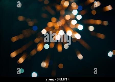 Bokeh sfocato di fuochi d'artificio esplode in strisce radiali di arancione e blu contro un cielo notturno scuro, creando un motivo astratto onirico. Foto Stock