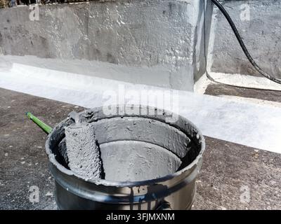 Primo piano di un rullo per verniciatura appoggiato in un secchio di vernice grigia per pareti durante un progetto di pittura e ristrutturazione all'aperto Foto Stock