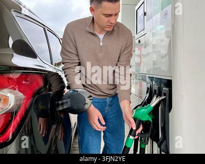 Giovane uomo che estrae un ugello di carburante verde da una pompa automatizzata alla stazione di servizio. Concetto di rifornimento self-service, spostamenti quotidiani in auto e energia moderna c Foto Stock
