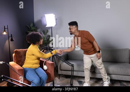 Ospite e ospitante afroamericani che si stringono la mano sul set di un podcast, micro a braccetto, cuffie, senape Foto Stock