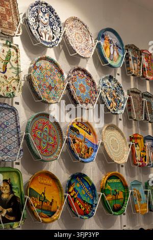3 luglio 2026: Budva, Montenegro, esposizione murale interna di piatti decorativi in ceramica colorati montati a griglia, con motivi floreali e scene di paesaggio Foto Stock