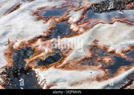 Una vista ad angolo alto mostra acqua sporca e macchie di ruggine che si diffondono su un lenzuolo di tessuto bianco all'aperto. Le pozzanghere formano macchie scure sul tessuto. Foto Stock