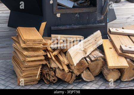 Pila di legna da ardere e assi di legno vicino a una stufa esterna Foto Stock