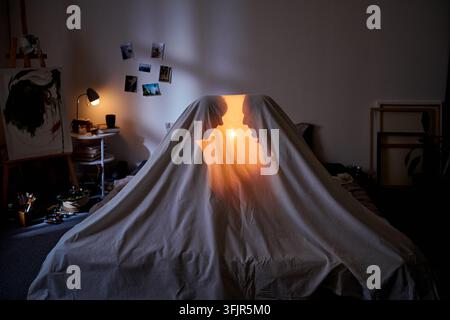 Coppia romantica nascosta sotto una coperta con la luce a casa Foto Stock