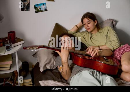 Coppia che si rilassa a casa mentre un uomo suona la chitarra acustica Foto Stock