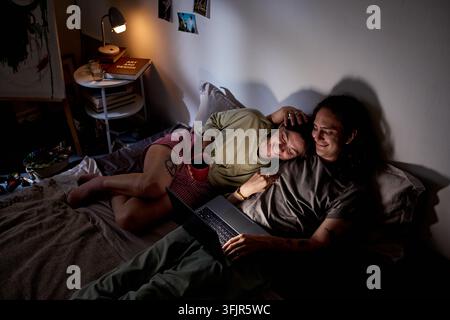 Coppia che si rilassa a letto guardando un film sul laptop di notte Foto Stock
