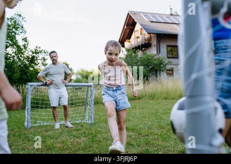 Famiglia che gioca a calcio insieme nel cortile sul retro durante l'estate. Foto Stock