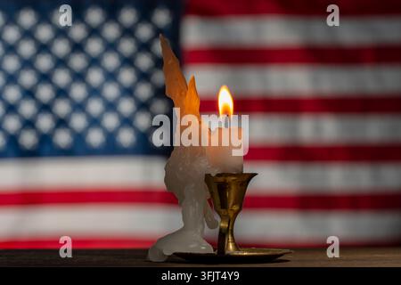 Candela accesa su sfondo sfocato della bandiera degli Stati Uniti, primo piano. Candela di cera bianca con fiamma luminosa brucia in un candelabro di metallo vintage su tavolo di legno con Foto Stock