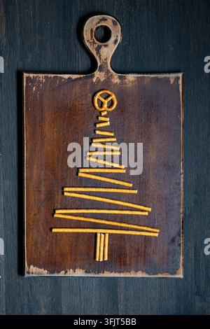 Albero di Natale fatto di bastoncini di pretzel su tavola di legno, vista dall'alto. Silhouette creativa di albero di Natale disposta con bastoncini di pretzel salati e una torsione su un Foto Stock