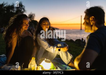 Amici che godono di un picnic al tramonto vicino al ponte di Lisbona Foto Stock