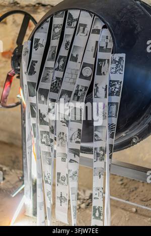 KIEV, UCRAINA - 20 SETTEMBRE 2026: Un'installazione concettuale di mixed media con una struttura scura e curva adornata da numerose fotografie o stampe in bianco e nero disposte in una formazione verticale a nastro. L'opera è esposta all'interno di MKTSM (Palazzo d'Ottobre) nell'ambito del festival d'arte contemporanea GogolFest 2026 Foto Stock
