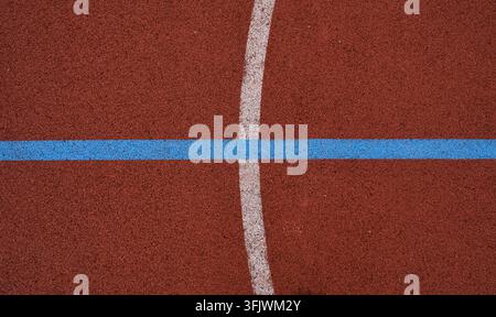 Superficie rossa testurizzata per piste sportive con linee bianche e blu audaci che si intersecano Foto Stock
