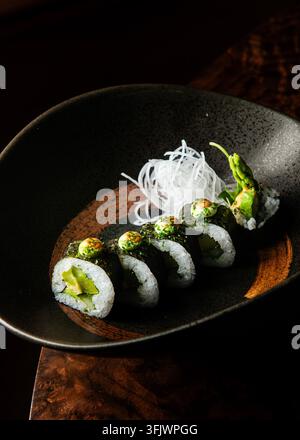 Vista laterale foto professionale di rotoli di sushi vegetali gourmet ripieni di asparagi e avocado, guarniti con salsa verde e ravanello daikon in Foto Stock