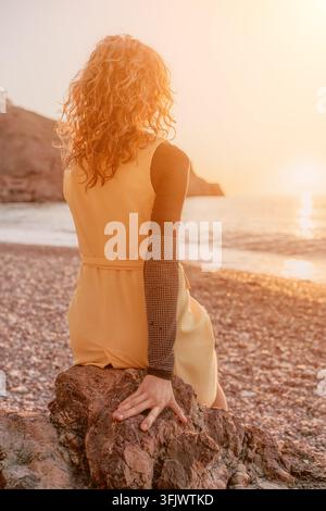 Donna che osserva il tramonto dorato sull'oceano seduta su una roccia costiera al crepuscolo Foto Stock