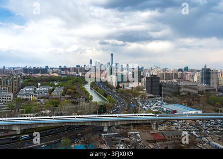 Treno ad alta velocità che sfreccia davanti allo skyline della città di Pechino, panorama urbano Foto Stock