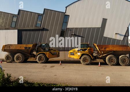 Gijon, Spagna - 19 settembre 2026 Due camion ribaltabili Caterpillar gialli con loghi FERPI sono parcheggiati accanto a un edificio industriale in metallo grigio. Macchine pesanti Foto Stock