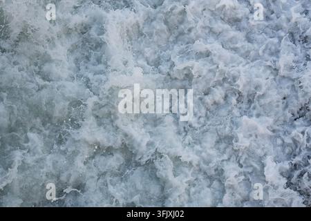 Prima piano astratta di schiuma bianca sull'acqua. La schiuma formata naturalmente crea una trama ariosa e dinamica adatta per sfondi Foto Stock